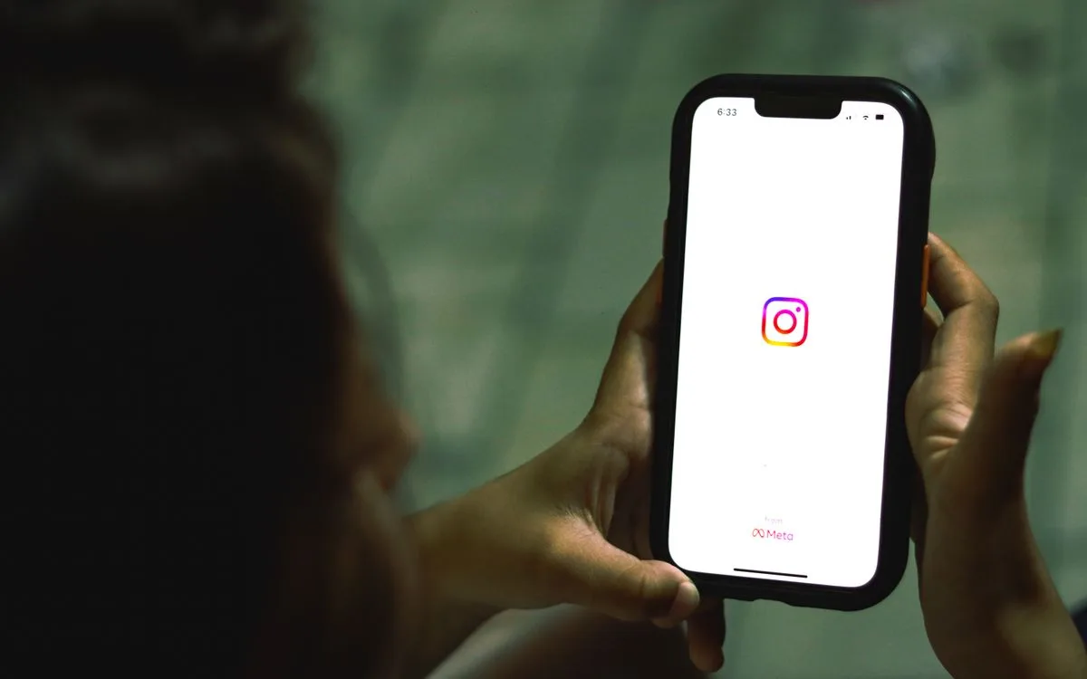 A hand holding a smartphone with the Instagram app icon on screen